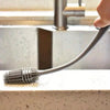 A silicone bottle brush with a long handle is shown resting on a countertop near a kitchen faucet.