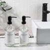 A set of clear glass soap dispensers with black pumps for dish soap and hand soap on a white countertop.