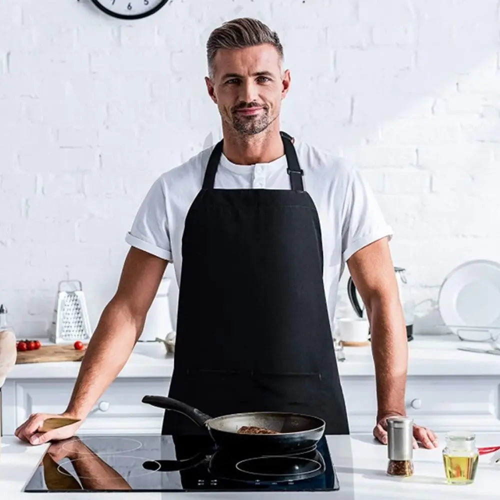 A man wearing a black chef apron stands in a kitchen, preparing food on a stovetop.