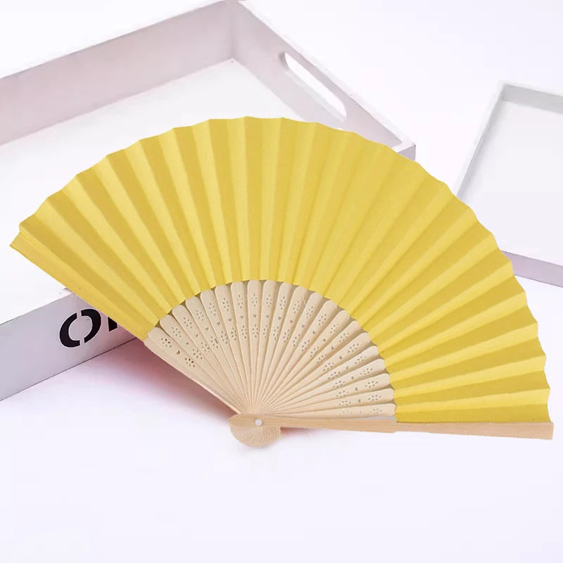 Un éventail pliable jaune en bambou et papier, montré en position semi-ouverte.