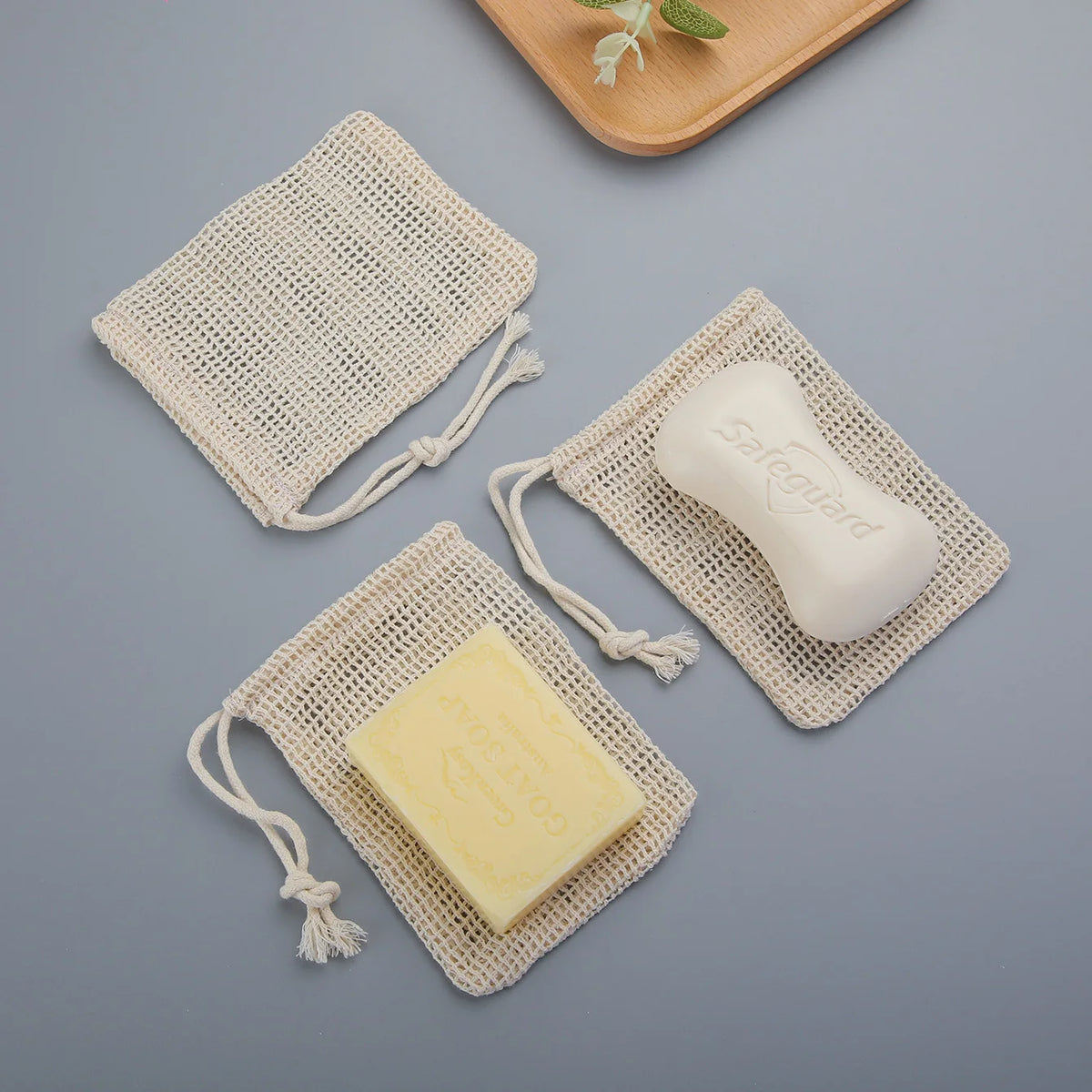 A set of natural cotton soap saver pouches containing a white bar of soap and a yellow soap block.