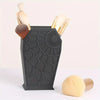 A black coffin-shaped makeup brush holder with a spider web design displaying several makeup brushes.