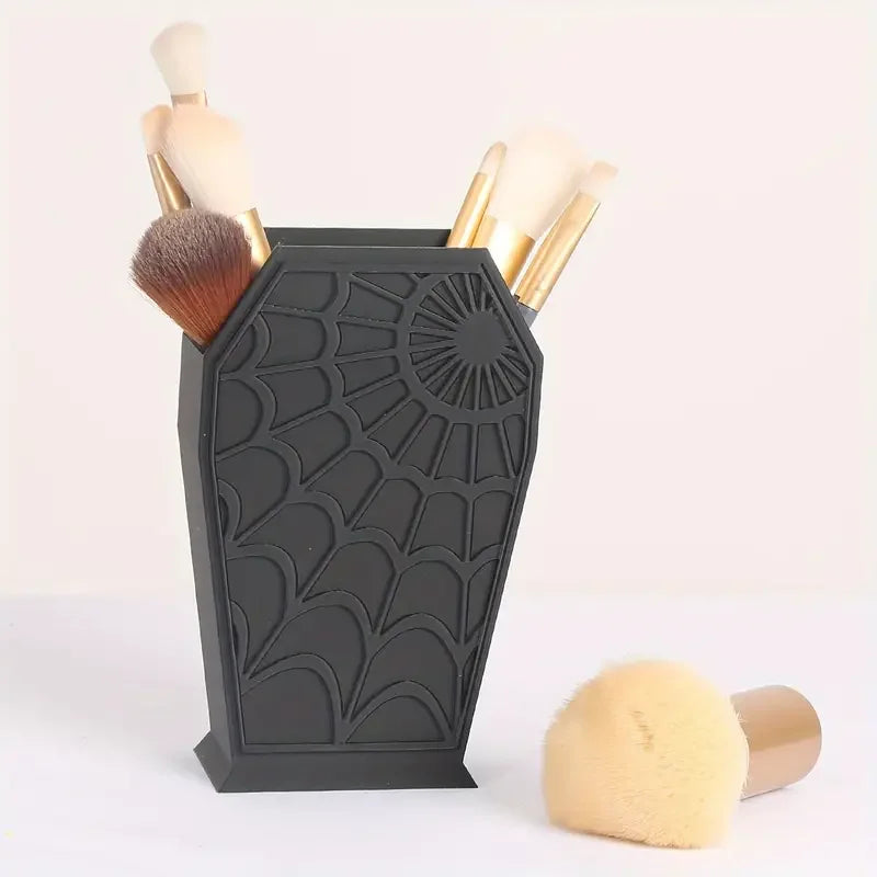A black coffin-shaped makeup brush holder with a spider web design displaying several makeup brushes.