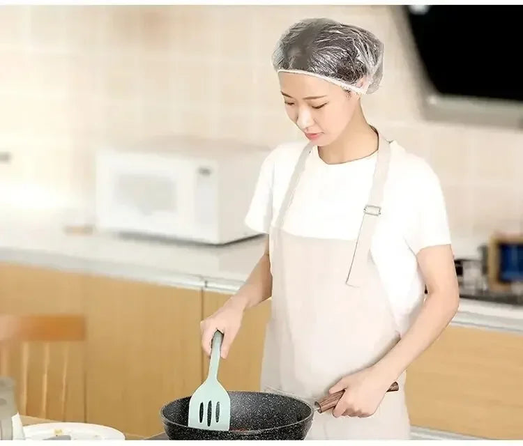 A woman wearing a reusable disposable shower cap is using a fork to stir food in a pan.