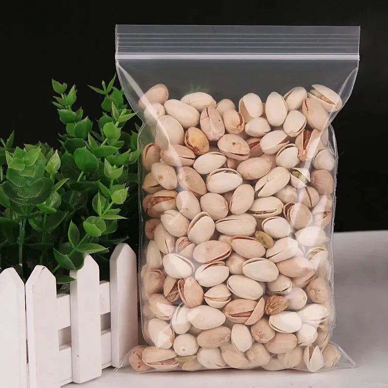 Una bolsa ziplock transparente llena de semillas o frutos secos beige claro, junto a una planta verde y listones de madera bl