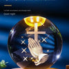 A clear crystal ball with a carved cross and praying hands inside, illuminated by warm light.