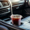 A clear disposable coffee cup filled with dark liquid is resting in a car's air vent cup holder.