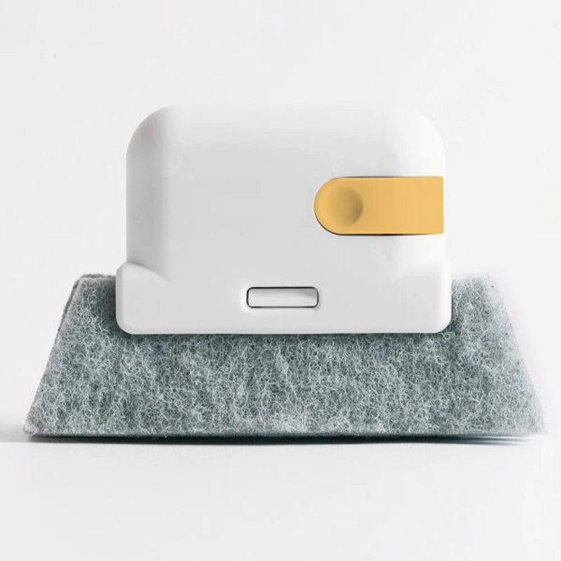 A white multi-purpose groove cleaning brush with a gold accent resting on a gray felt surface.