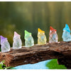 A row of luminous resin mini fairy gnomes in various pastel colors rests on a piece of weathered wood.