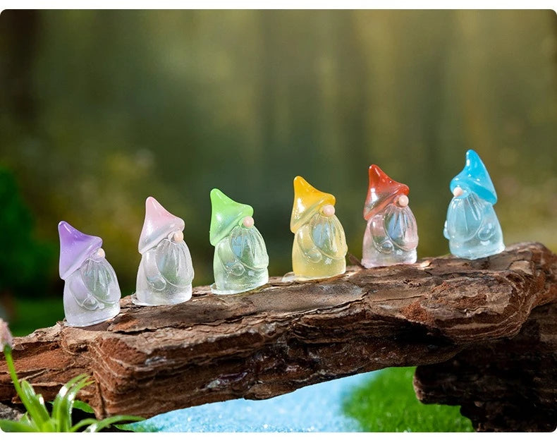 A row of luminous resin mini fairy gnomes in various pastel colors rests on a piece of weathered wood.