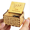 An antique wooden hand crank music box with a lid featuring musical notes and the text Over the Rainbow is held in a hand.