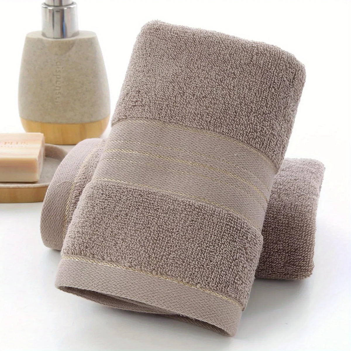 A stack of soft, beige bath towels with gold trim and a wooden bottle in the background.