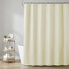 A cream-colored waffle weave shower curtain hanging from a metal rod in a bathroom setting.