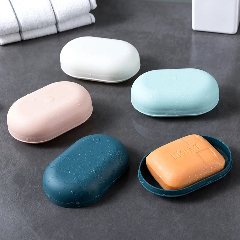 Five portable soap holders in various pastel colors including white, pink, blue, and orange resting on a dark surface.