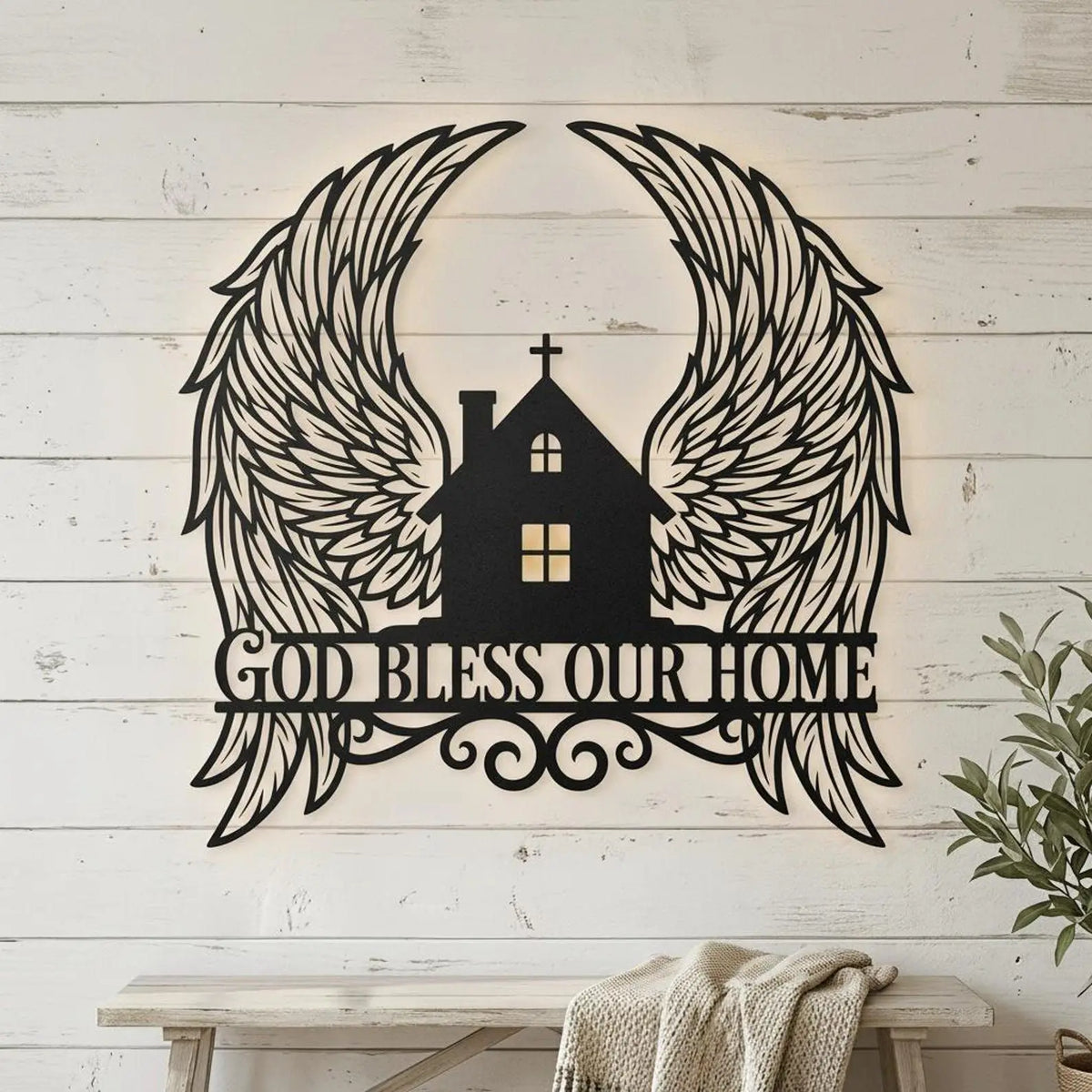 Black metal wall art featuring a silhouette of wings surrounding a house with a cross and the text God Bless Our Home