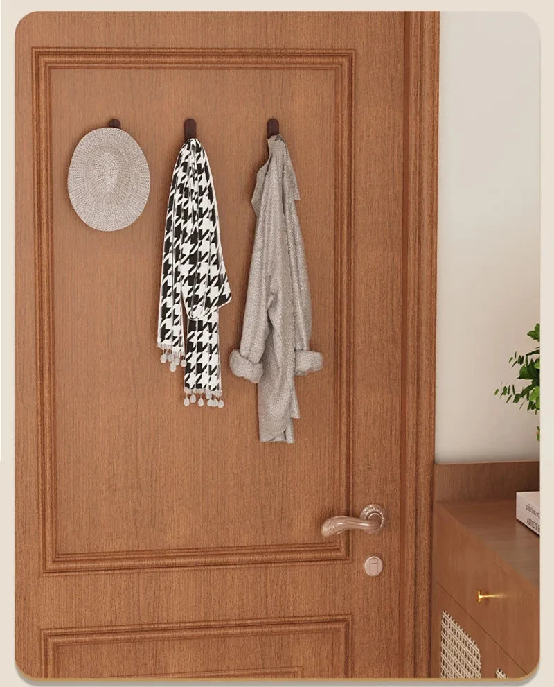 A wooden door features wall hooks displaying a black and white patterned scarf and a gray towel.