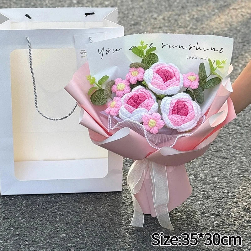 A handmade crochet flower bouquet featuring pink and white roses and greenery, presented in a pink paper wrap.