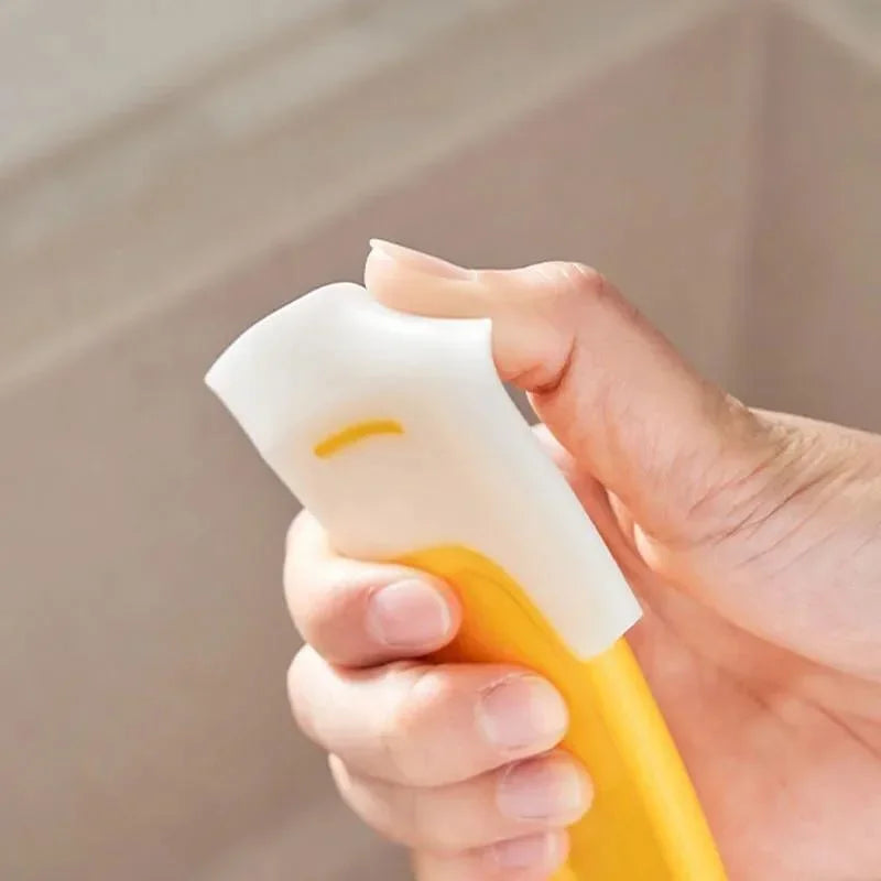 A hand holds a yellow silicone kitchen scraper used for cleaning pots and dishes.