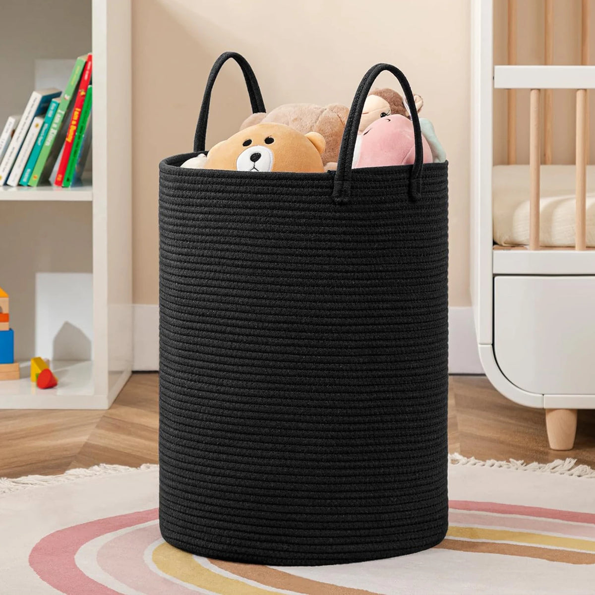 A large black woven storage hamper with handles filled with soft stuffed animals sits on a rug.