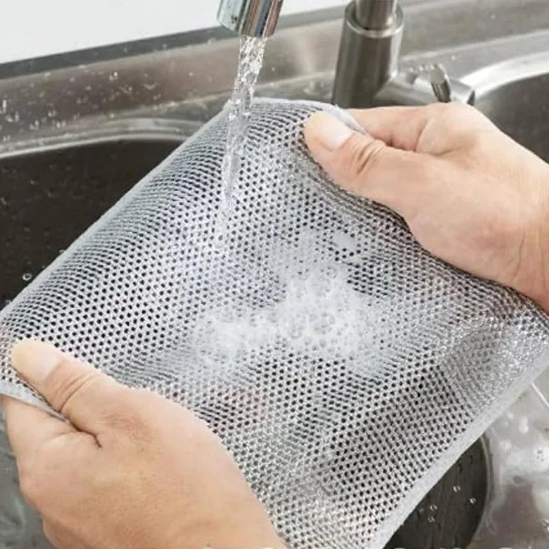 A hand is squeezing a mesh steel wire cleaning cloth into a sink, showing water being squeezed out.