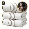 A stack of three white bath towels with gold stripes, showing a close-up of one towel.