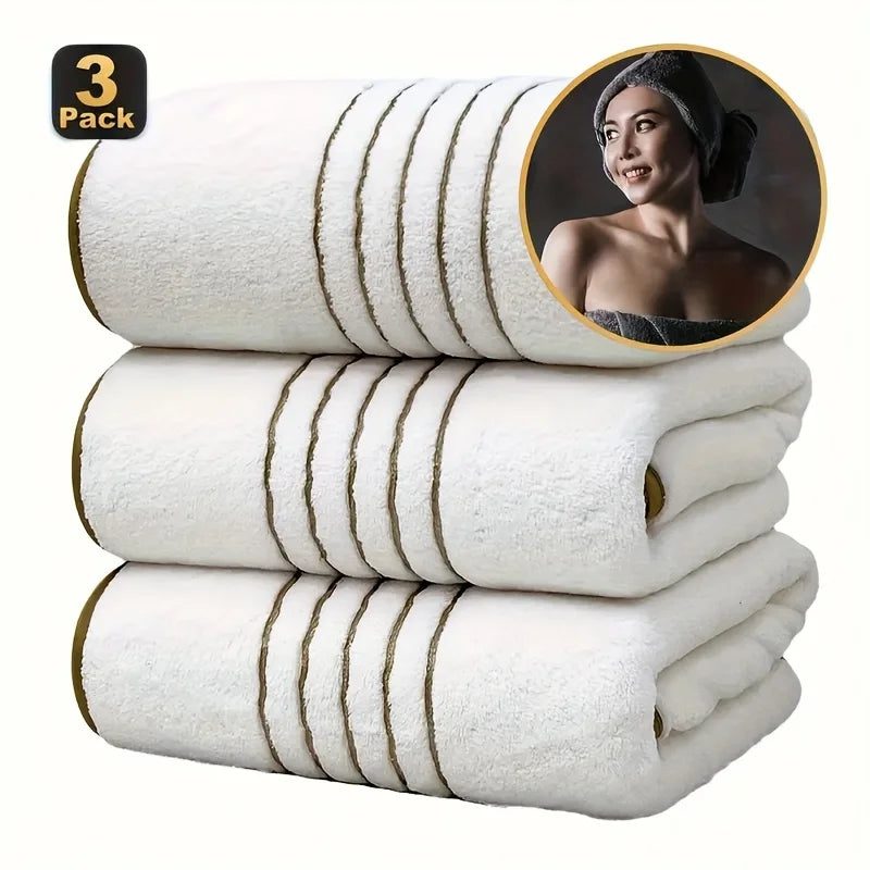 A stack of three white bath towels with gold stripes, showing a close-up of one towel.