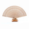 Un éventail pliable beige clair en bois de santal avec de délicates perforations, exposé sur un support en bois.