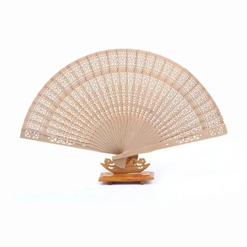 Un éventail pliable beige clair en bois de santal avec de délicates perforations, exposé sur un support en bois.