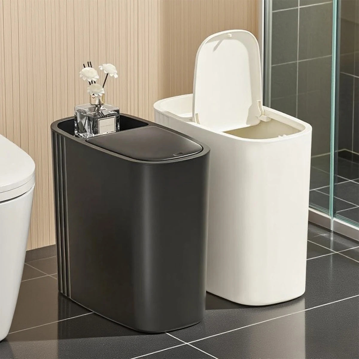 A modern gray trash can with a press lid is shown next to a white toilet.