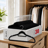 A box of black non-slip velvet hangers with chrome hooks is displayed on a wooden surface next to a closet rack.