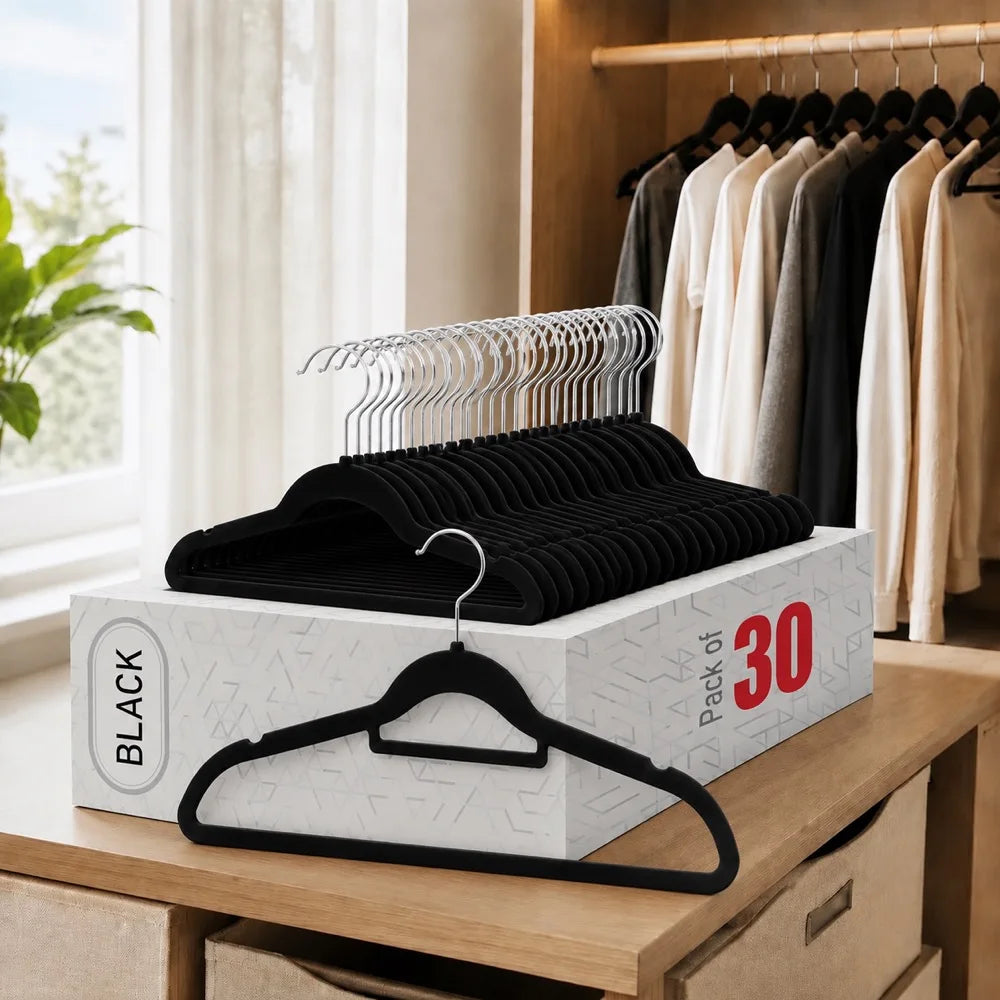 A box of black non-slip velvet hangers with chrome hooks is displayed on a wooden surface next to a closet rack.