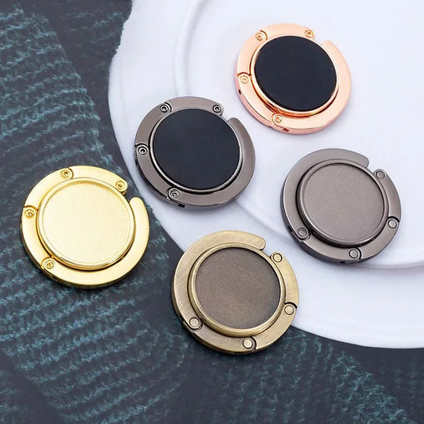 A set of four compact folding bag hangers or organizers in gold and black colors arranged on a white plate.