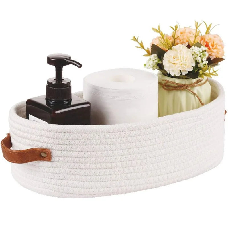 A white woven cotton storage basket holds a roll of toilet paper and a bouquet of flowers.