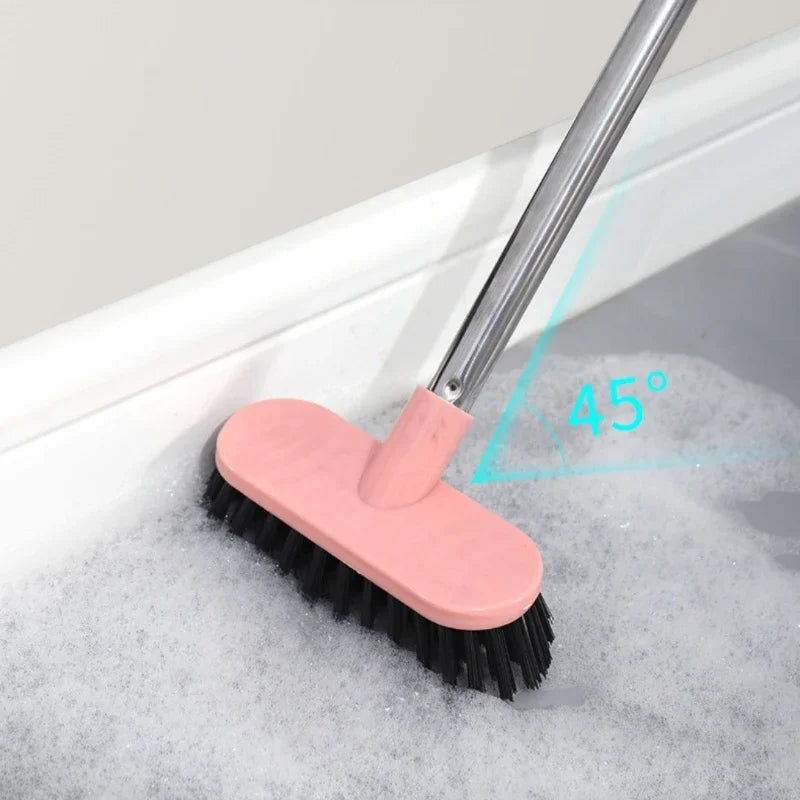 A pink heavy-duty long-handle floor scrub brush is shown scrubbing foam in a bathtub, demonstrating a 45-degree angle.