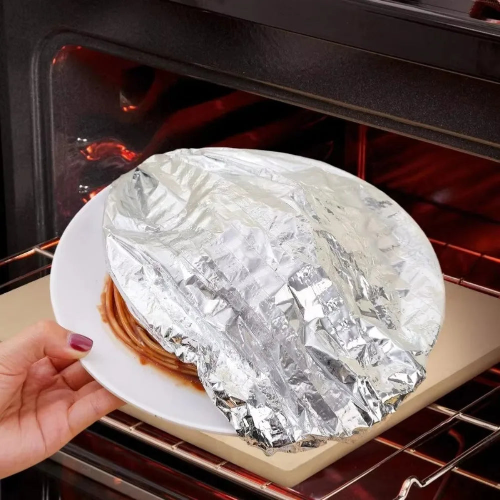 A hand holds a piece of food wrapped in aluminum foil inside an oven or cooking appliance.