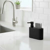 A black dish soap dispenser with a sponge holder sits on a white countertop next to a kitchen faucet.