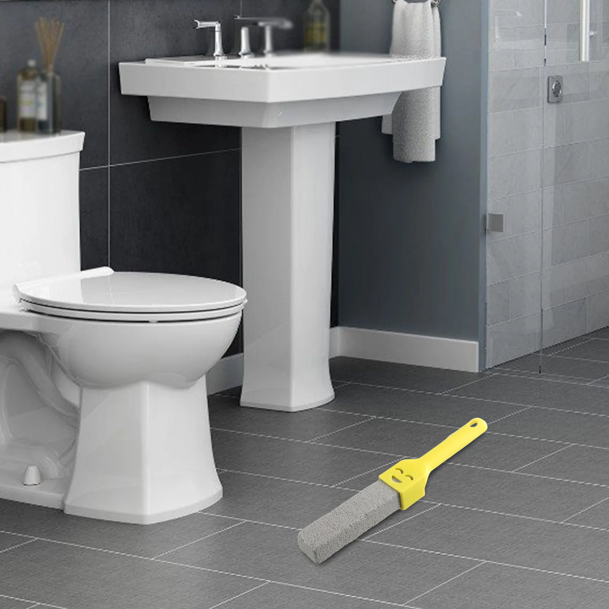 A natural pumice toilet cleaning brush with a yellow handle is shown next to a white sink and toilet.