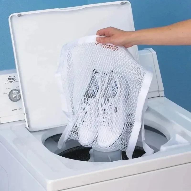 A hand places a white reusable mesh laundry bag for shoes into the drum of a white washing machine.