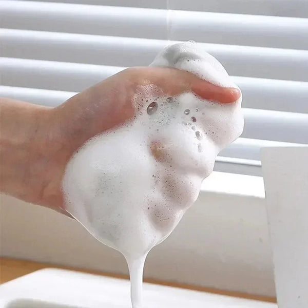 A hand is squeezing a thick, white cleaning foam or soap lather against a window blind.