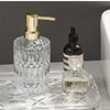 Klares Glas-Seifenspenderflasche mit goldfarbener Pumpen-Oberseite und einer kleinen Glasflasche daneben.