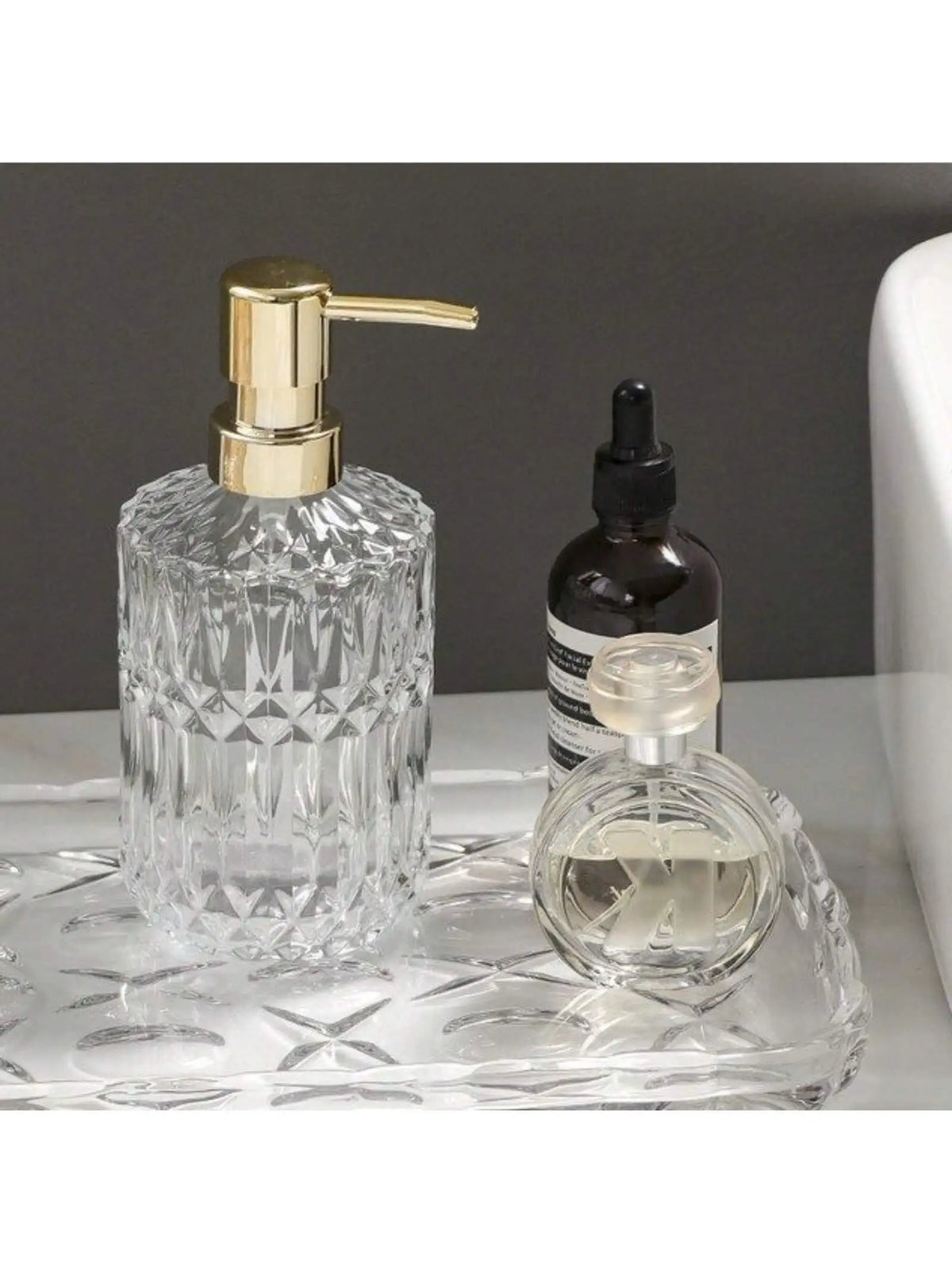 Klares Glas-Seifenspenderflasche mit goldfarbener Pumpen-Oberseite und einer kleinen Glasflasche daneben.
