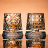Un par de vasos de whisky facetados con líquido ámbar sobre una superficie reflectante.