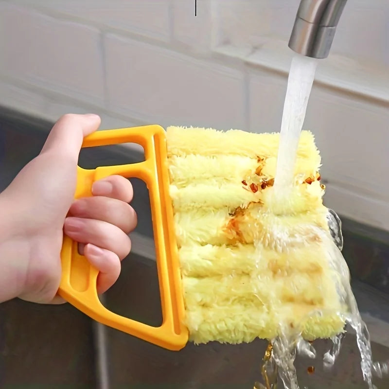 A hand is using a yellow detachable window blind cleaning brush to spray water onto a surface.