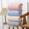 A stack of thickened microfiber bath towels in pink, blue, cream, and gray resting on a wooden surface.