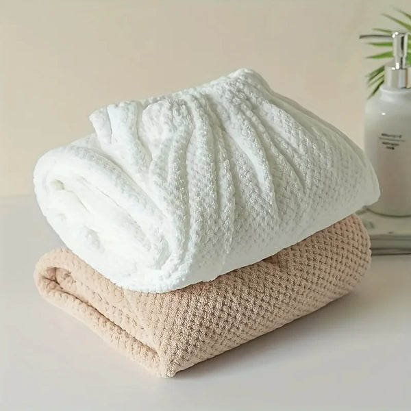 Ein Stapel weißer Mikrofasertücher und ein beige Handtuch auf einer weißen Oberfläche.