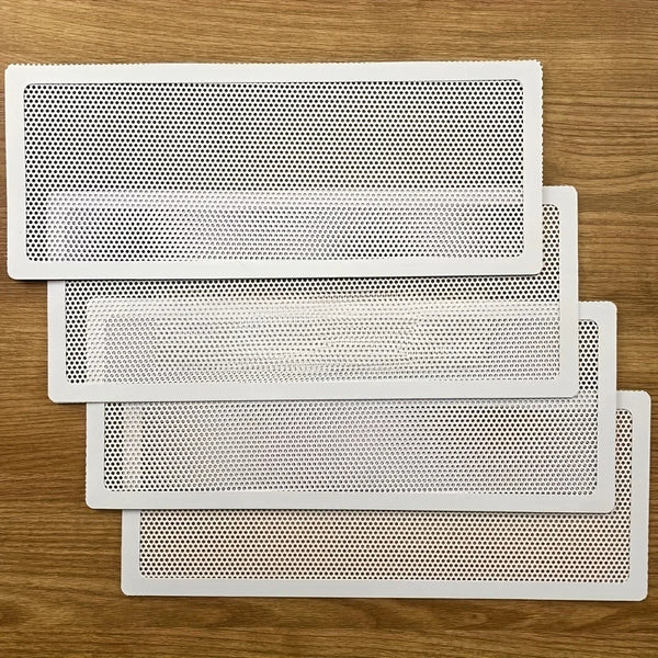 Vier weiße magnetische Lüftungsabdeckungen oder Filter mit perforiertem Netzmuster auf einer Holzoberfläche.