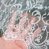 A hand is holding white lace retro tablecloth fabric with intricate floral patterns.