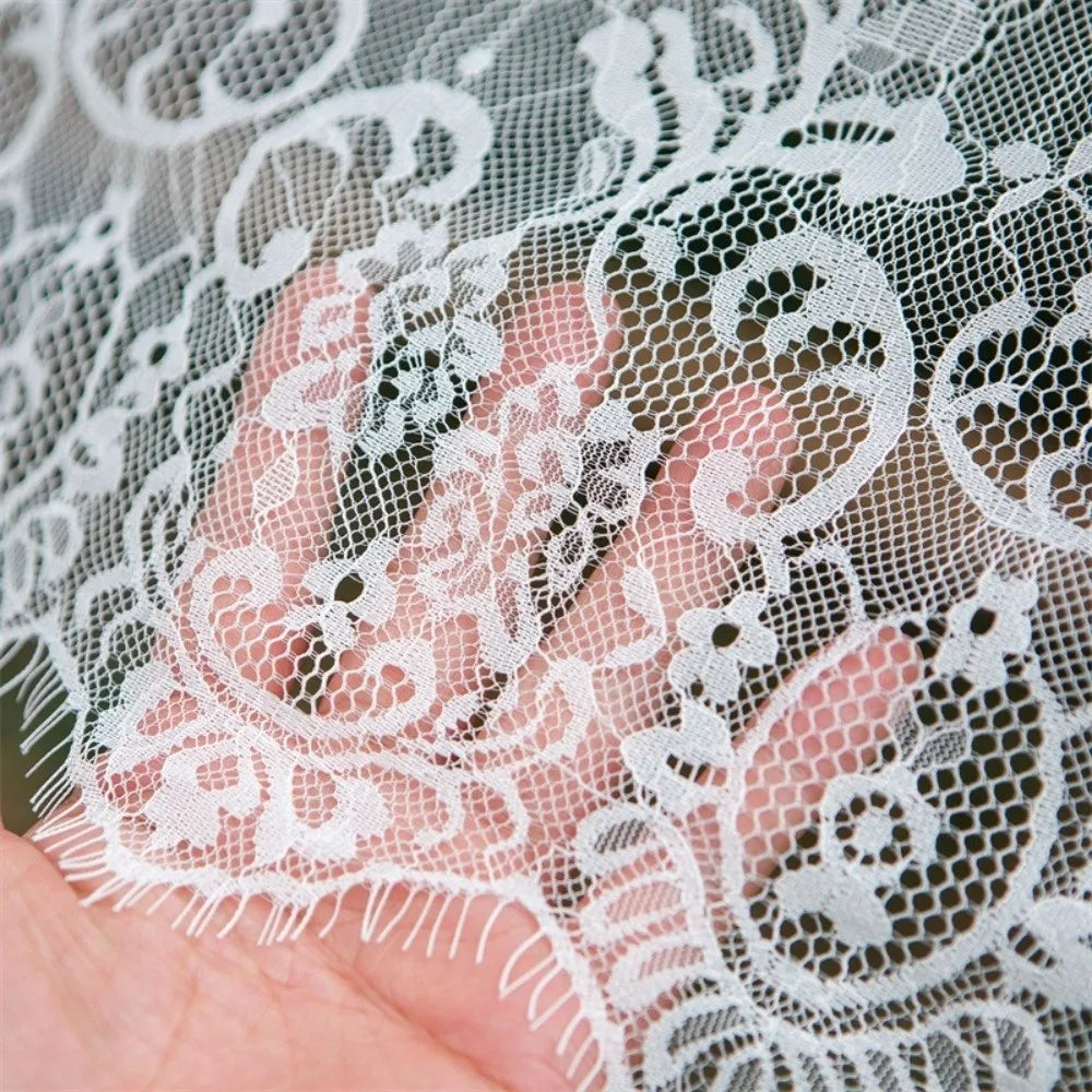 A hand is holding white lace retro tablecloth fabric with intricate floral patterns.