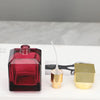 A dark red glass perfume spray bottle next to a gold-colored metal applicator and cap.