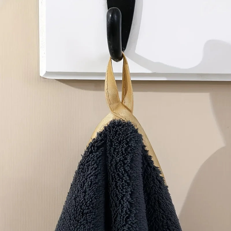 A black coral fleece towel hanging from a black hook with a gold stripe detail.